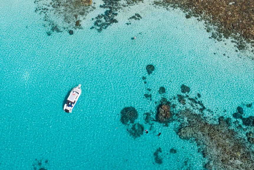 Aerial shot looking down on a white boat over blue water and rocky corals